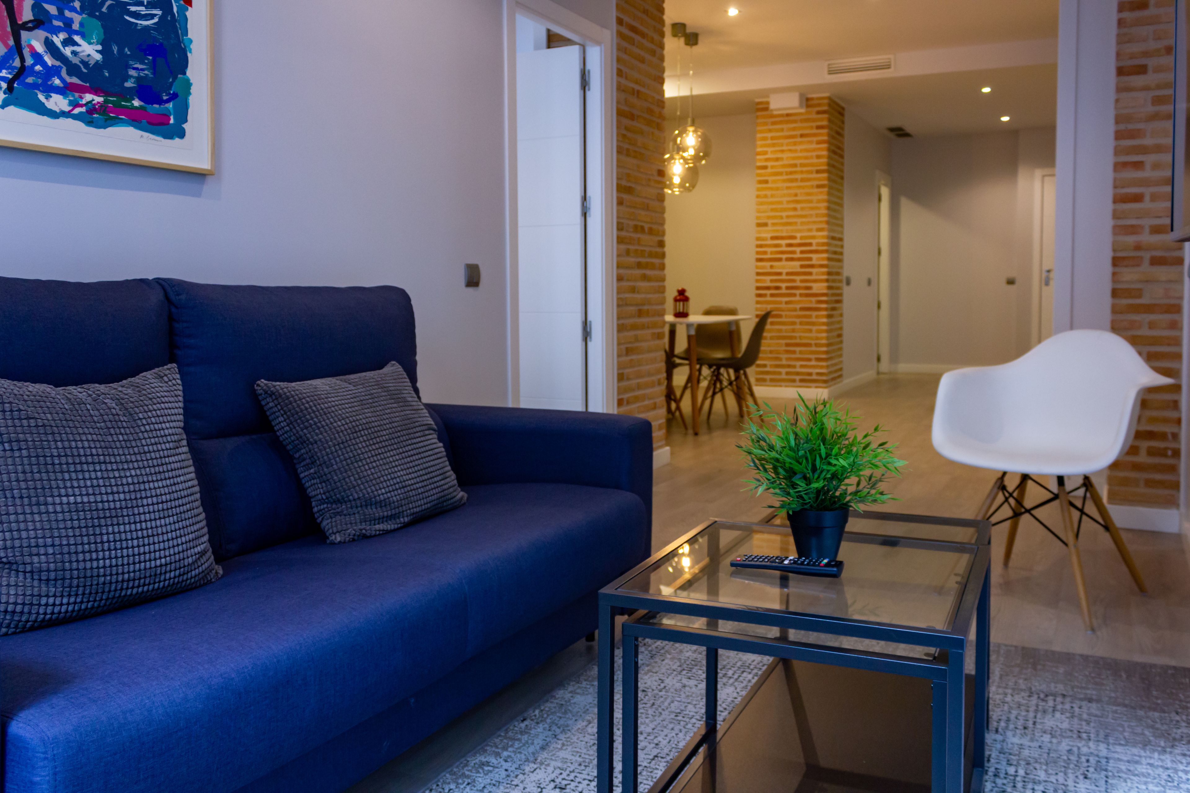 Un salon moderne avec un canapé bleu, une table basse en verre et un fauteuil blanc.