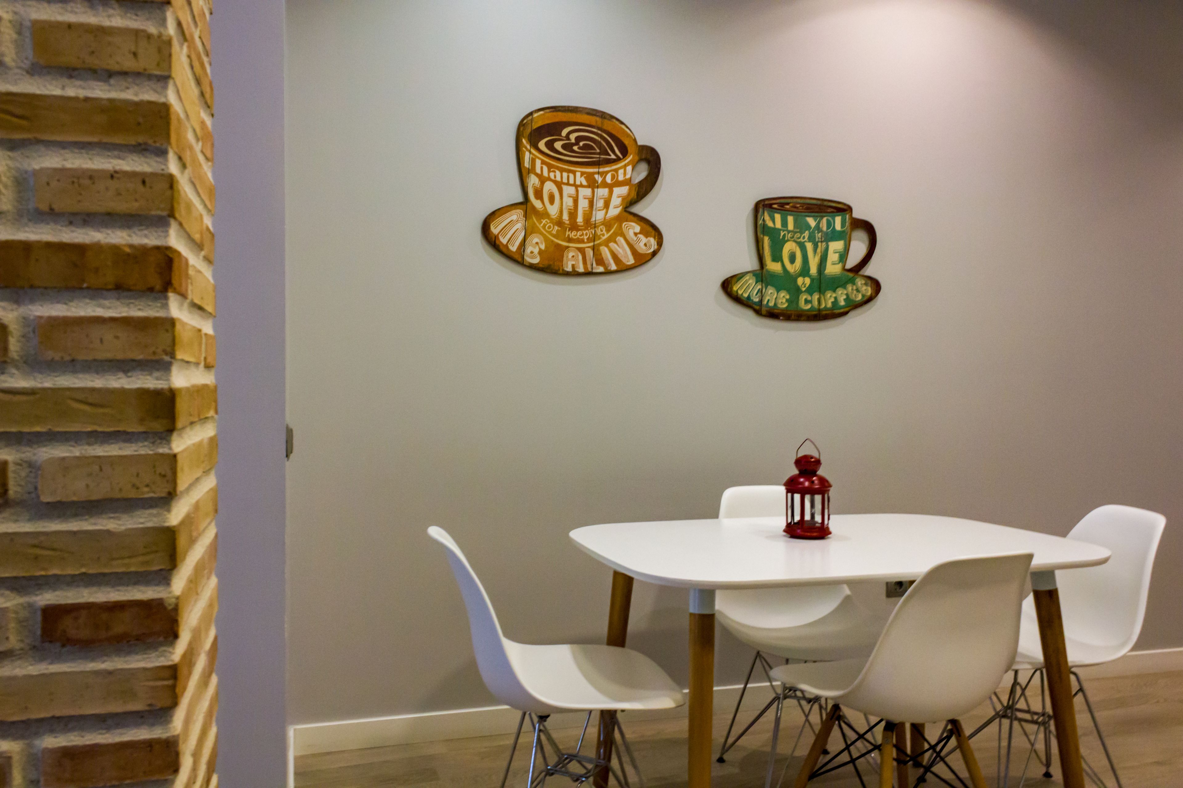 Un comedor con una mesa y sillas blancas, una pared de ladrillo y dos adornos de pared.