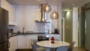 A modern kitchen with white cabinets, a stainless steel range hood, and a round dining table with four chairs. - Arenal Suites (Madrid)