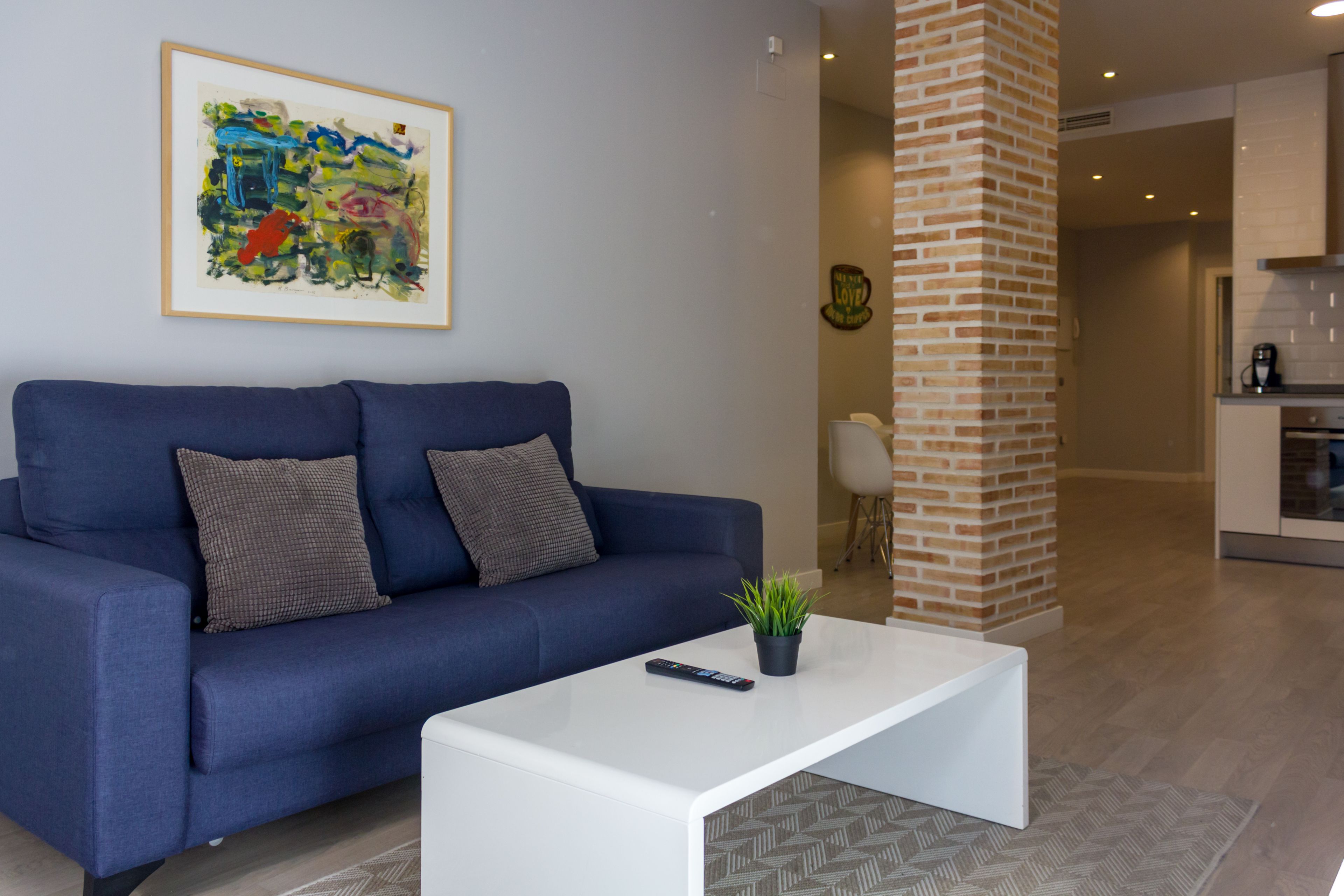 Una sala de estar moderna con un sofá azul, una mesa de centro blanca y un cuadro abstracto enmarcado en la pared.