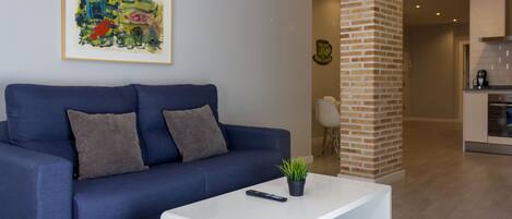 Una sala de estar moderna con un sofá azul, una mesa de centro blanca y un cuadro abstracto enmarcado en la pared.
