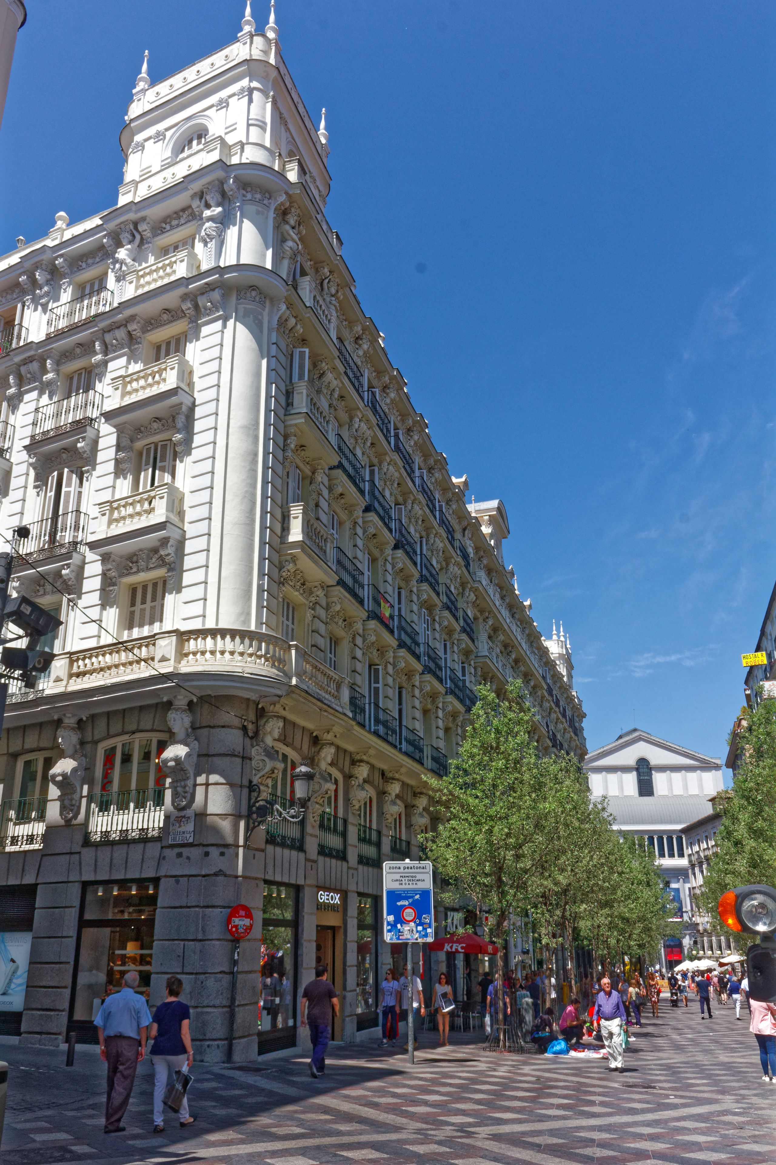 Un edificio histórico con arquitectura ornamentada, un restaurante KFC y una calle peatonal con gente caminando.