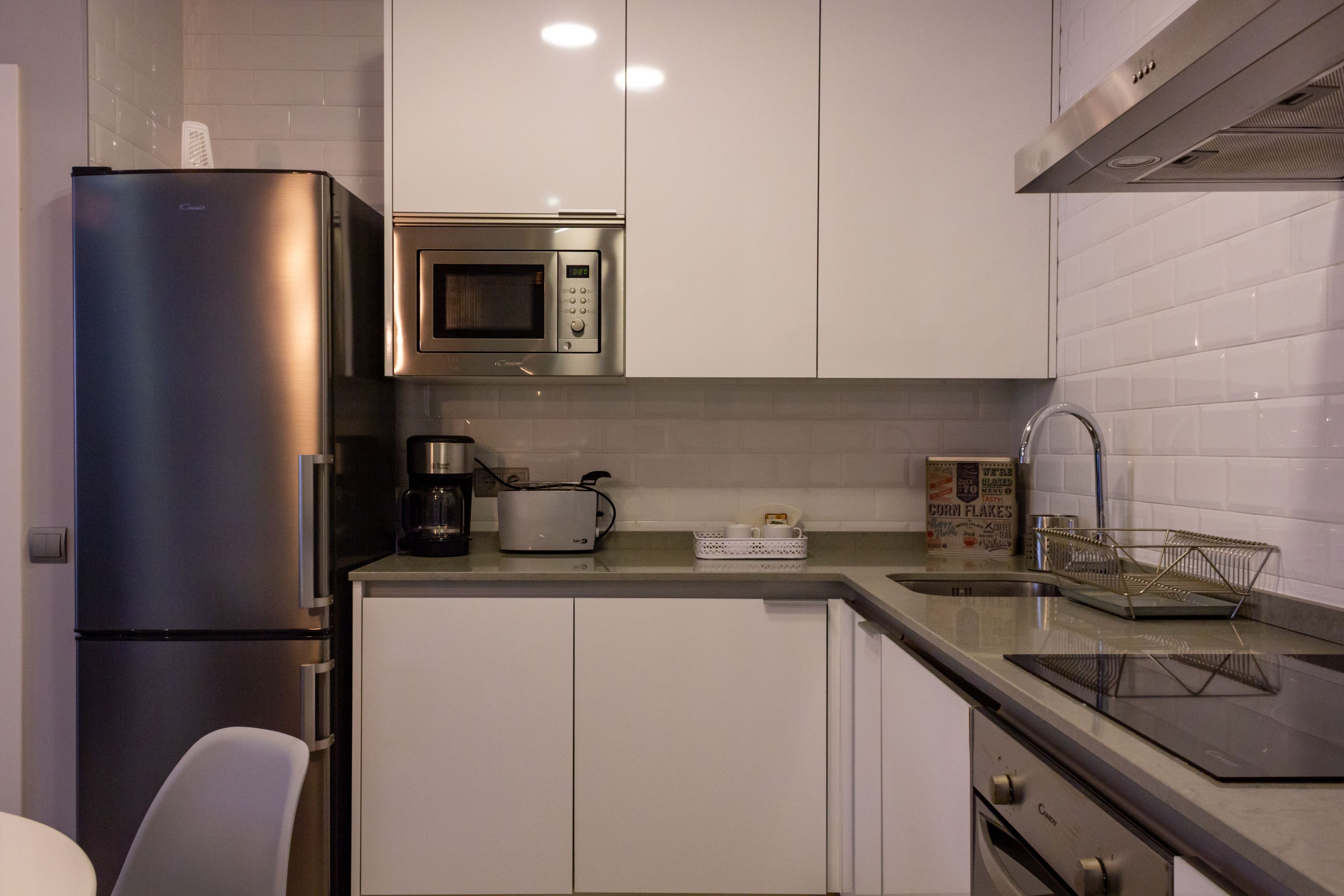 A modern kitchen with stainless steel appliances, white cabinetry, and a countertop with a coffee maker, toaster, and cereal box.