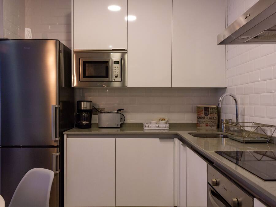 A modern kitchen with stainless steel appliances, white cabinetry, and a countertop with a coffee maker, toaster, and cereal box.