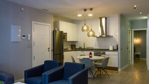 A modern kitchen with white cabinets, a stainless steel refrigerator, and a dining area with blue chairs and a round table. - Arenal Suites (Madrid)