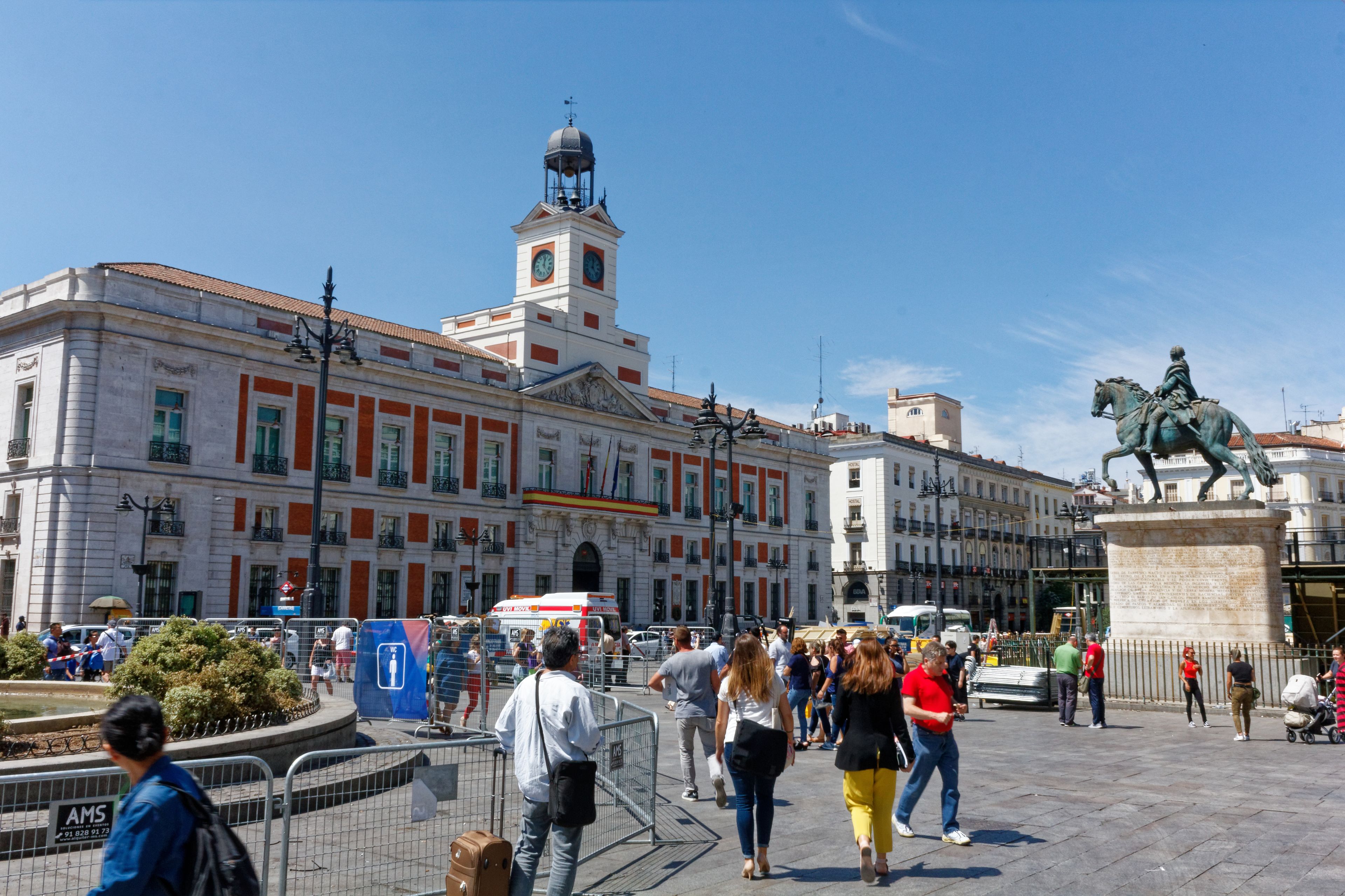A public square with a prominent building featuring a clock tower and a statue of a figure on horseback.