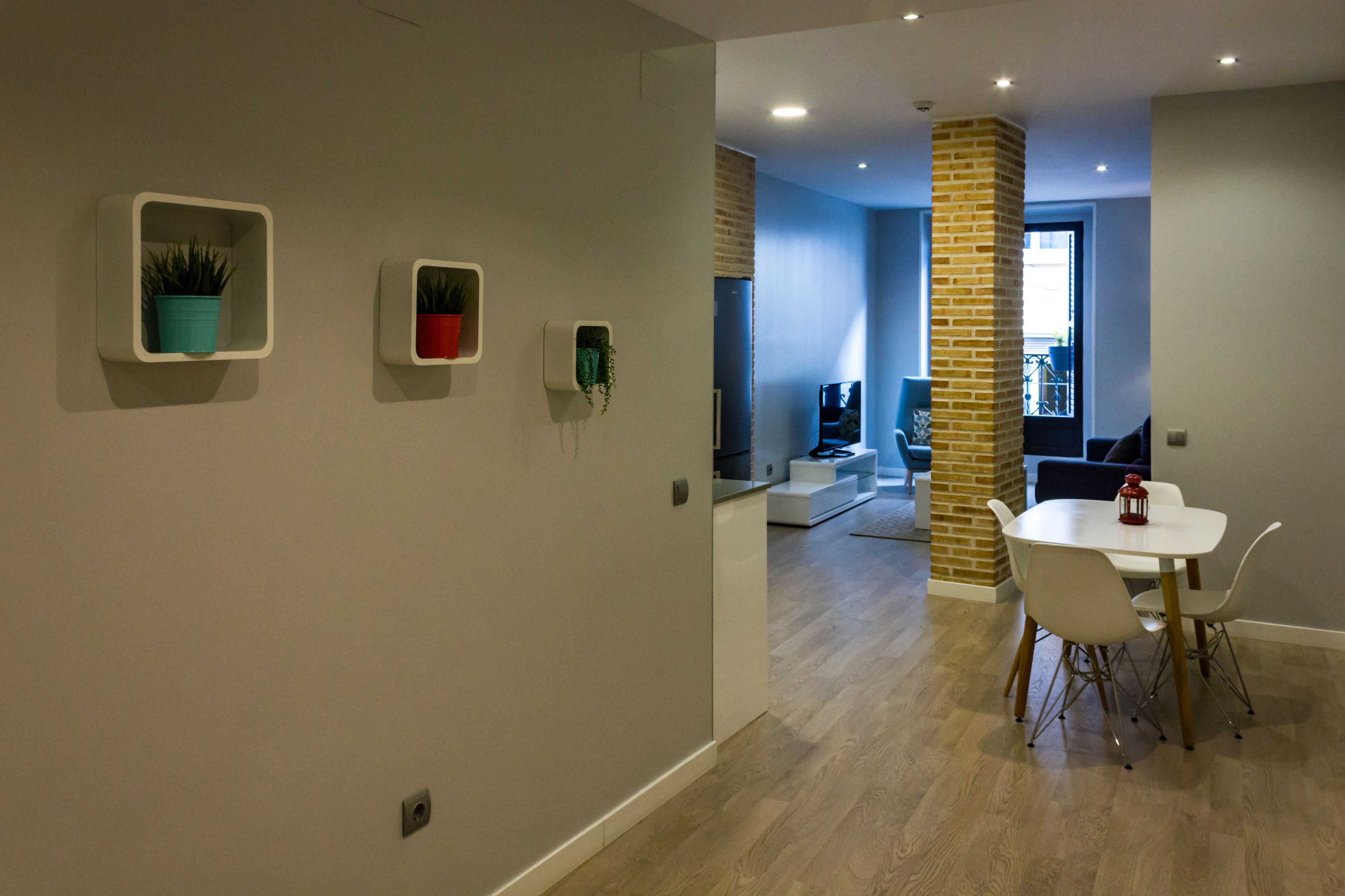 A modern dining area with a white table and chairs, a brick pillar, and potted plants on the wall.
