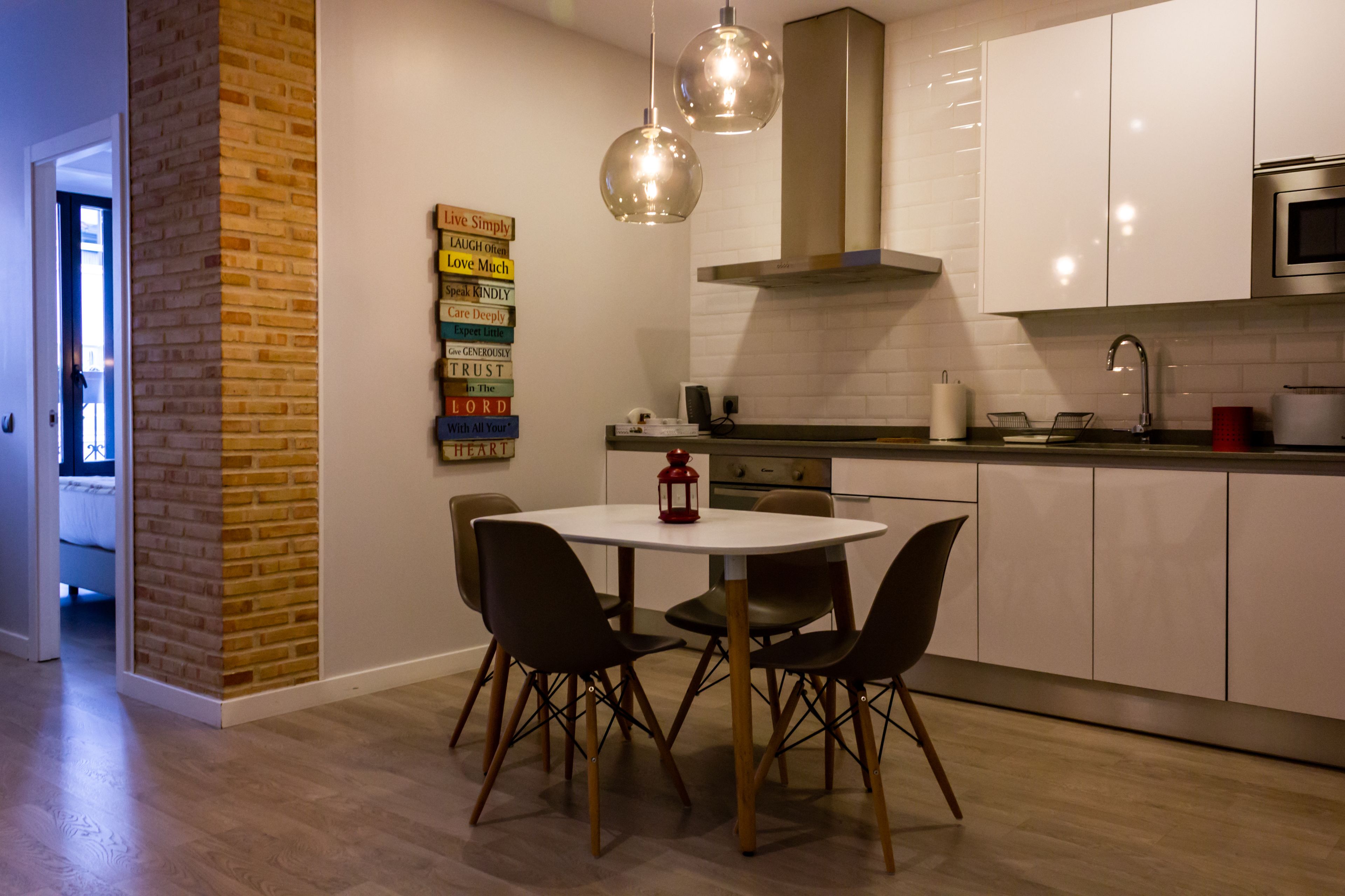 Una cocina moderna con armarios blancos, una mesa redonda de comedor con cuatro sillas y una pared de ladrillo decorativa.