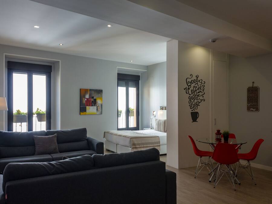 Una sala moderna con un sofá, una mesa de comedor con sillas rojas, una cama y una zona de cocina.