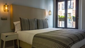 A neatly made bed with patterned bedding, a bedside table, and a hanging light fixture. - Arenal Suites (Madrid)