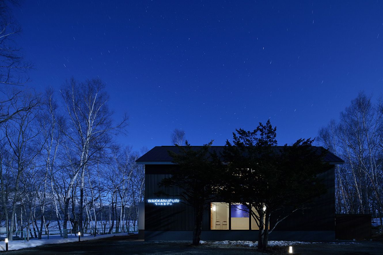 A modern building with a sign reading "WAKKANUPURI" at night, surrounded by trees and a snowy landscape.