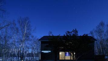 A modern building with a sign reading "WAKKANUPURI" at night, surrounded by trees and a snowy landscape.