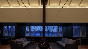 A modern living room with a fireplace, two sofas, and large windows offering a view of a lake and trees. - Wakkanupuri (Teshikaga)