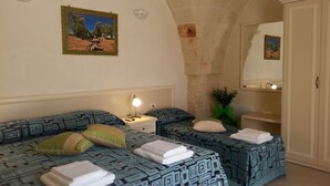 A room with two beds, each with patterned bedding and pillows, a nightstand with a lamp, a small plant, and a mirror on the wall. - B&B Demetra (Carovigno)