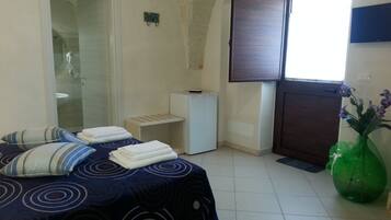Une chambre à coucher comprenant un lit, une petite table de chevet, un espace douche et une fenêtre avec des rideaux.
