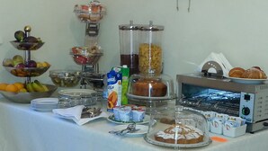 A buffet table with various food items, including fruits, a juice cooler, a bread display, and a microwave. - B&B Demetra (Carovigno)