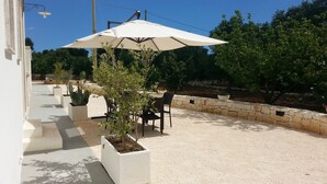 An outdoor patio area with a table and chairs under a large umbrella, surrounded by potted plants and a stone wall. - B&B Demetra (Carovigno)