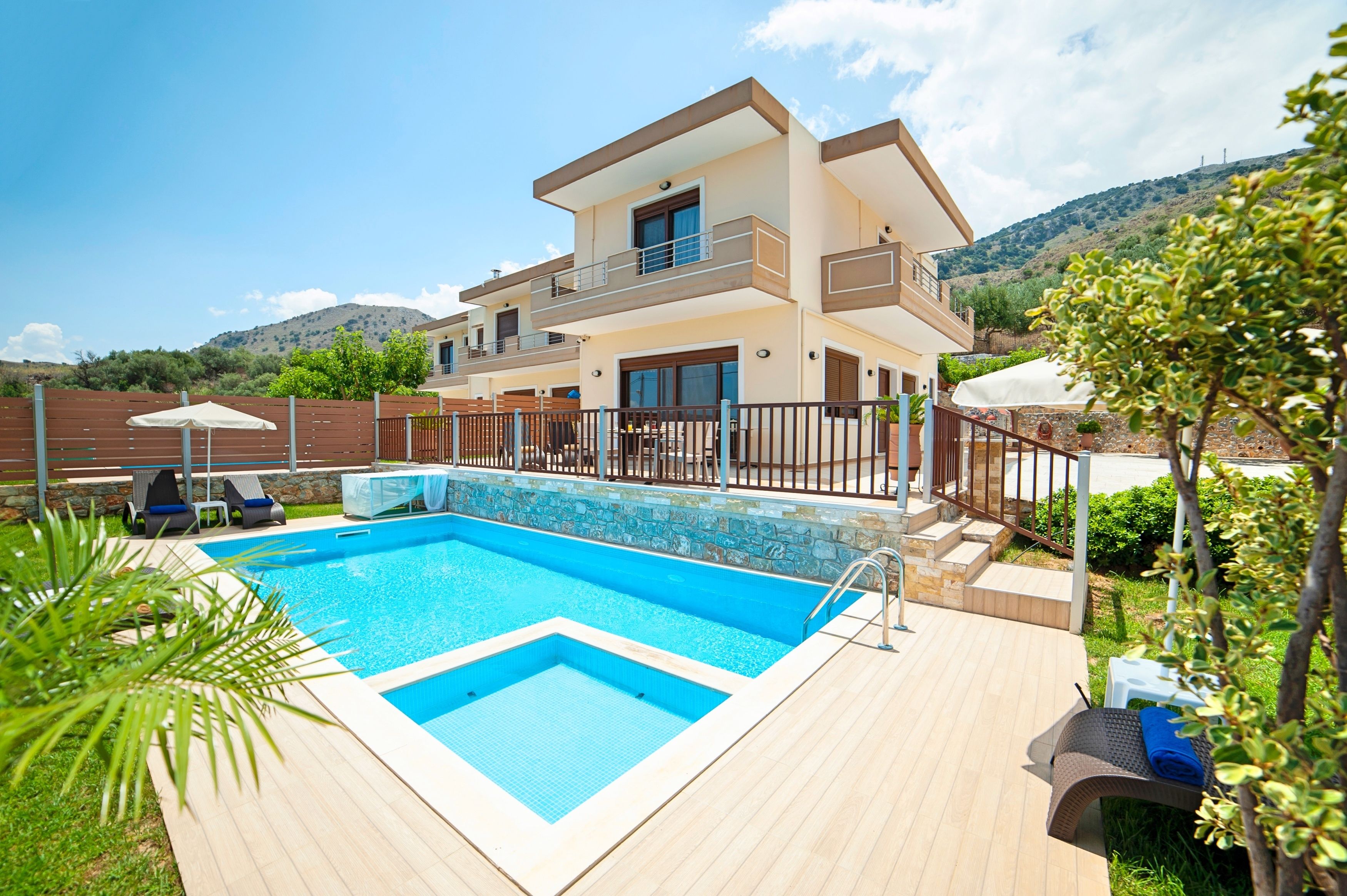 A modern two-story house with a swimming pool, a covered patio, and a view of hills.