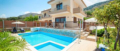 A modern two-story house with a swimming pool, a covered patio, and a view of hills.