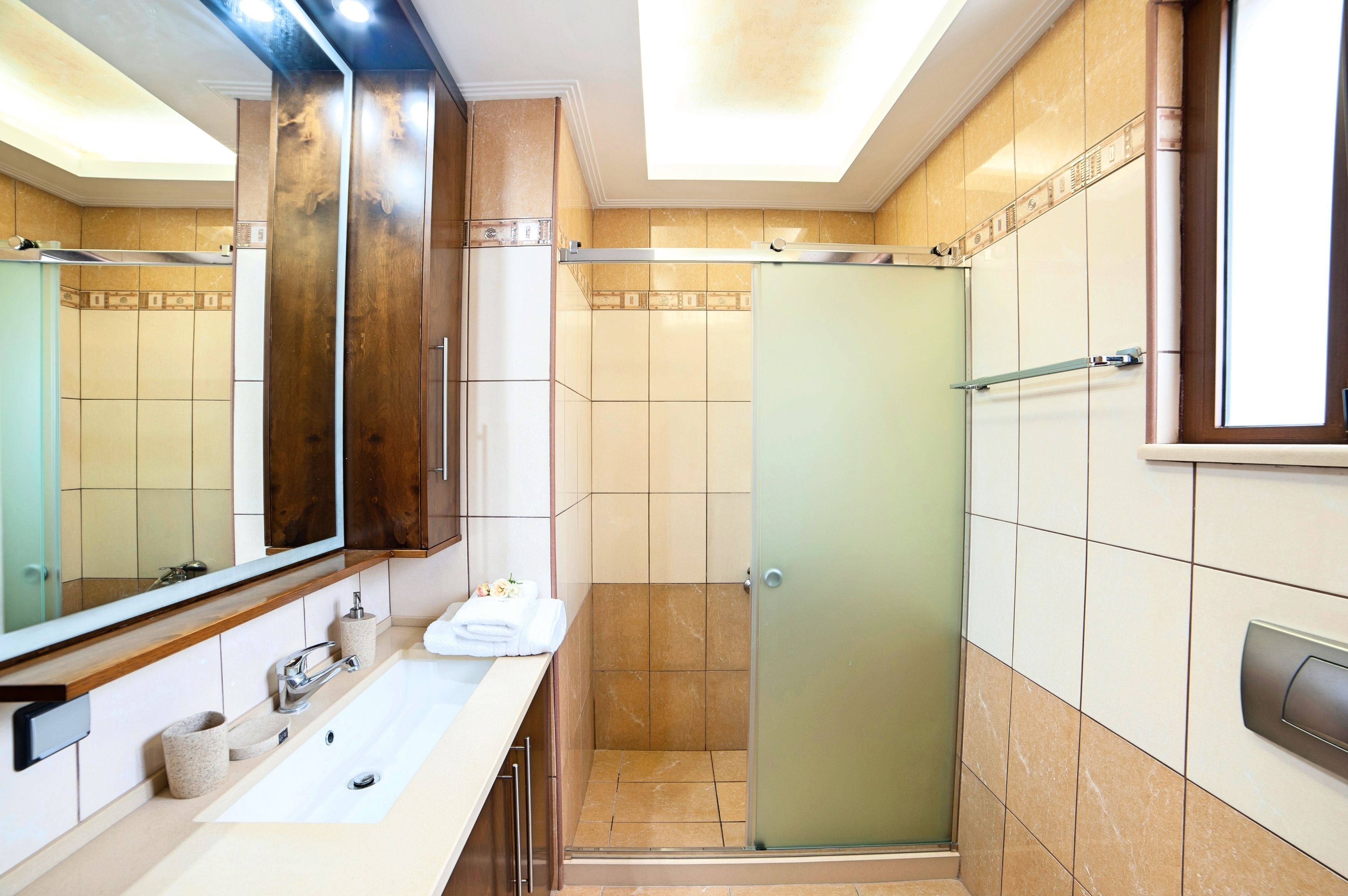 A modern bathroom with a large mirror, a sink, a shower, and a toilet.
