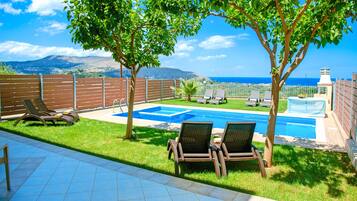 Relax by the pool surrounded by lush greenery and a clear sea view, with lounge chairs and a dining table at your disposal.