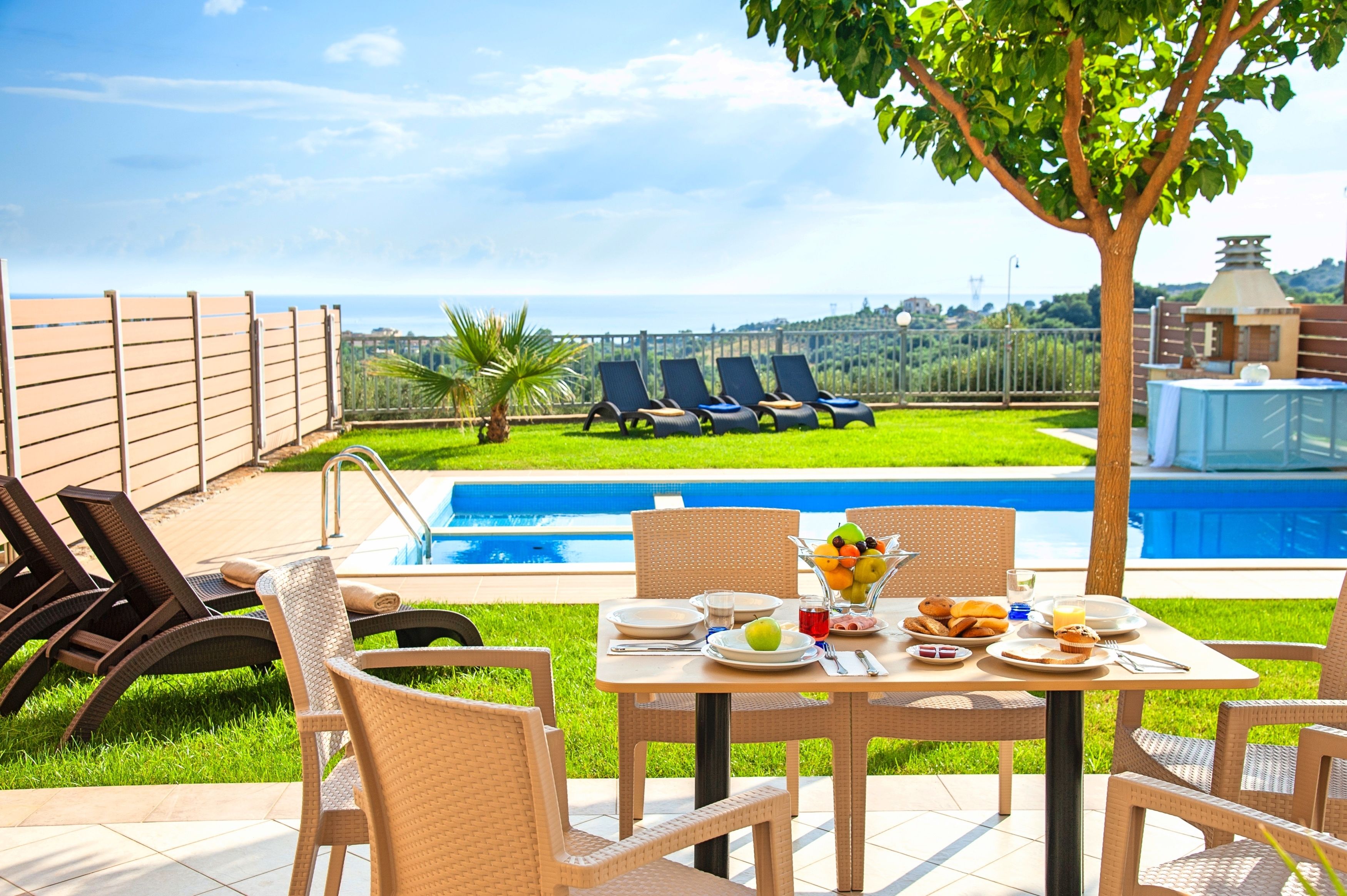 A poolside dining area with a table set for breakfast, overlooking a swimming pool and a scenic view.