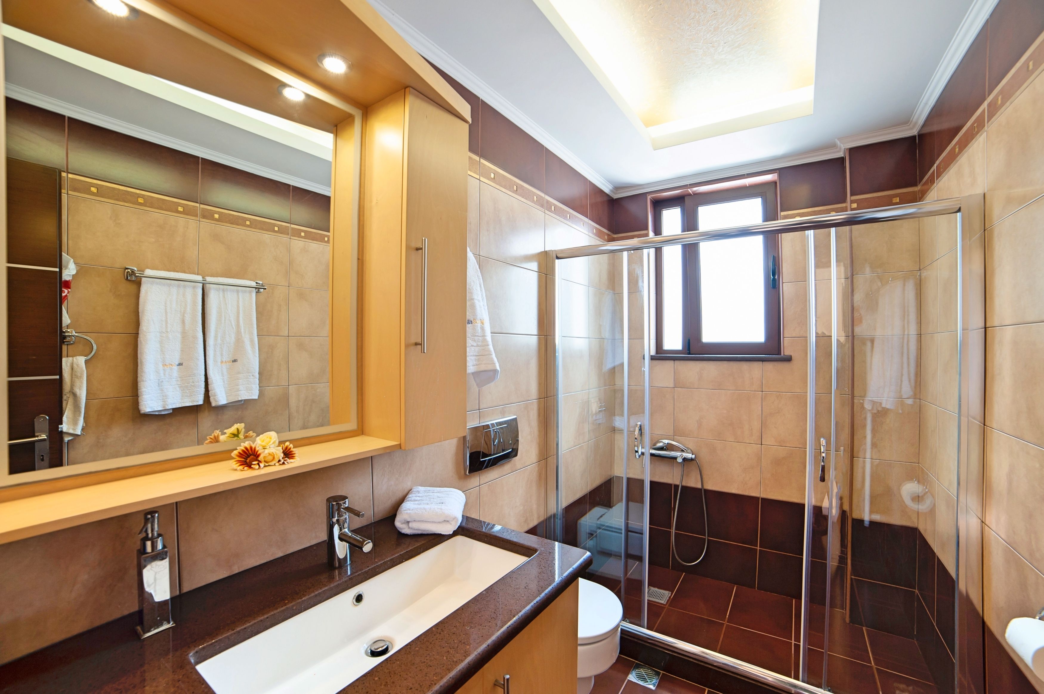 A modern bathroom with a large mirror, a sink, a toilet, and a glass-enclosed shower.