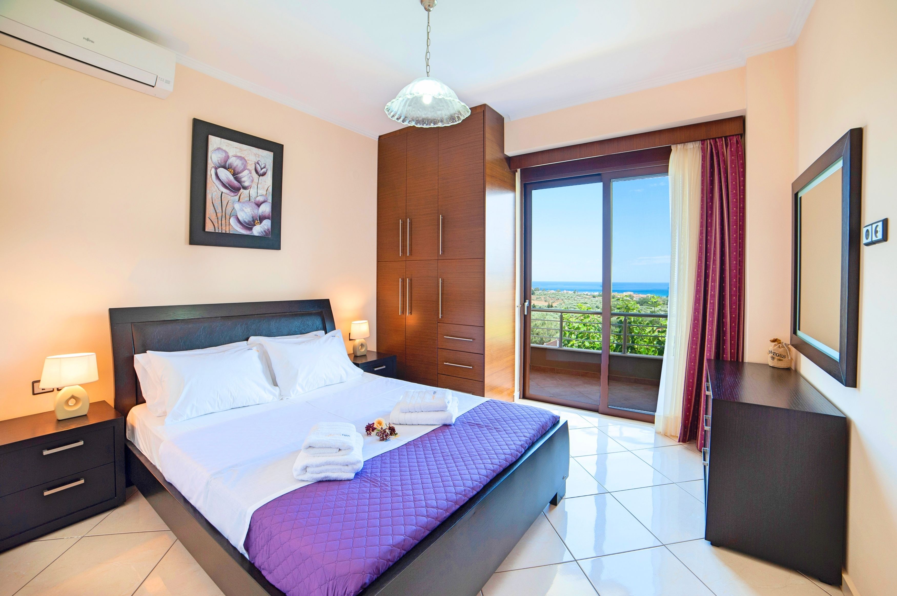 Une chambre d’hôtel comprenant un lit, une table de chevet, une lampe, une grande fenêtre avec vue et un ventilateur de plafond.