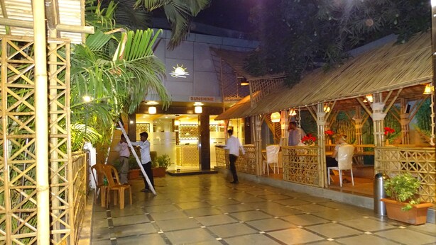 Un patio interior con suelo de cuadros, estructuras de bambú y una zona de restaurante con sillas y mesas.
