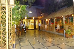 Une cour intérieure dotée d’un sol à carreaux, de structures en bambou et d’un espace restaurant avec des chaises et des tables.