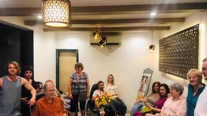 Un grupo de personas en un interior moderno con una araña, unidades de aire acondicionado y un panel decorativo en la pared.