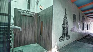 Un pasillo con una puerta de madera con la etiqueta 'Sunshine Backpackers Dormitory' y un mural de un templo en la pared.