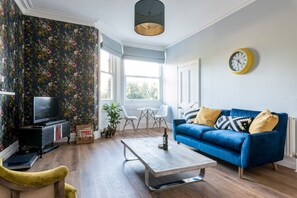 A living room with a blue sofa, a wooden coffee table, a television, and a floral wallpaper.