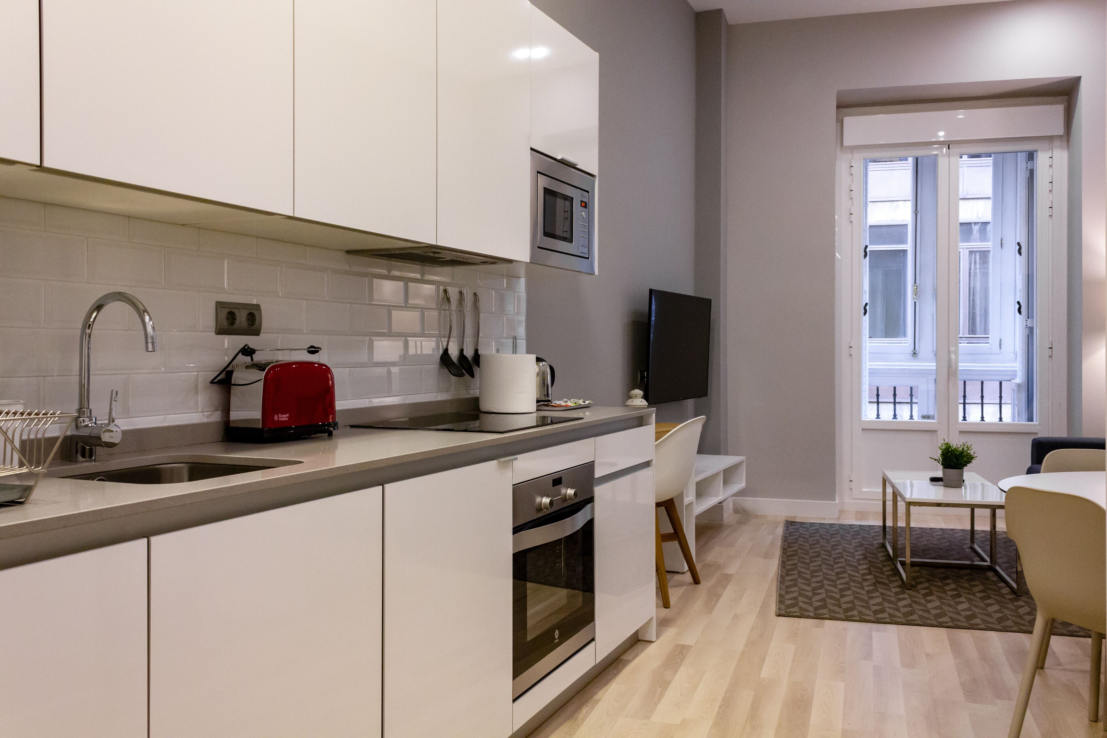 Una cocina moderna con armarios blancos, una tostadora roja, un microondas y un televisor sobre el mostrador.