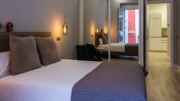 Habitación de hotel moderna con una cama grande, lámparas de noche, una mesita y vistas al balcón y la cocina.