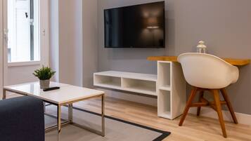 A modern living room with a flat-screen TV mounted on the wall, a white coffee table, a dark sofa, a wooden side table, and a white chair.