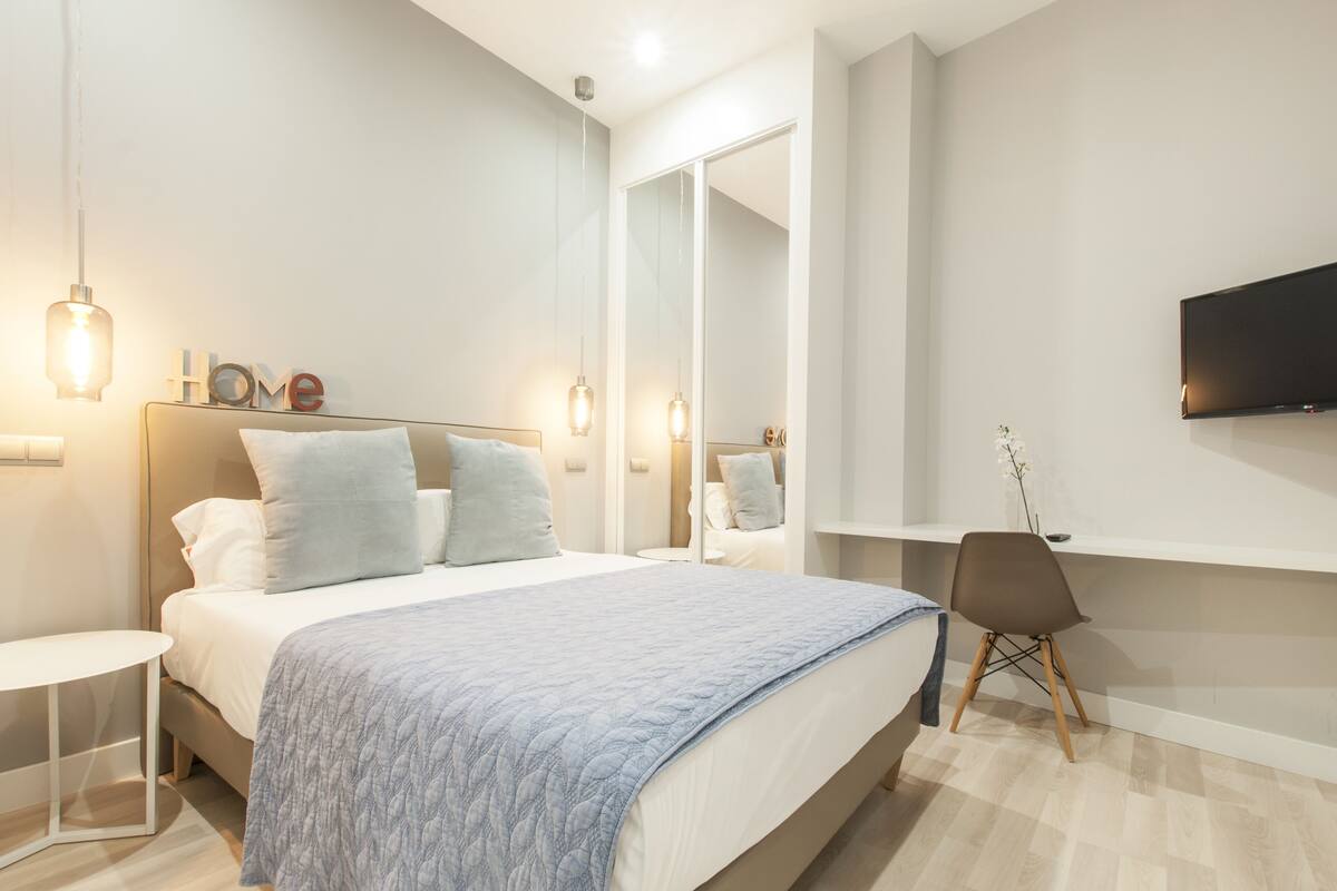 A modern bedroom with a bed, bedside tables, a chair, a TV, and a mirror.