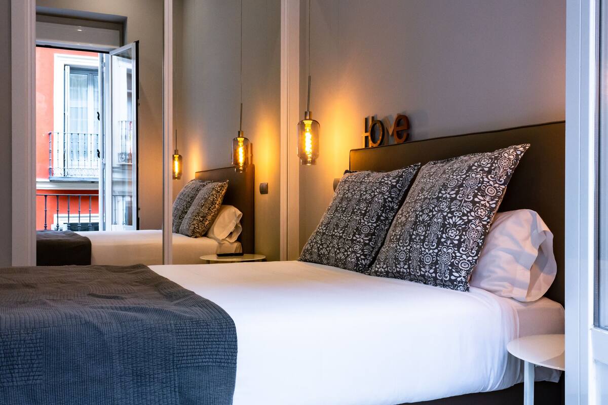 A modern hotel room with a large bed, two bedside tables, a nightstand, a mirror, and a view of the outside balcony.