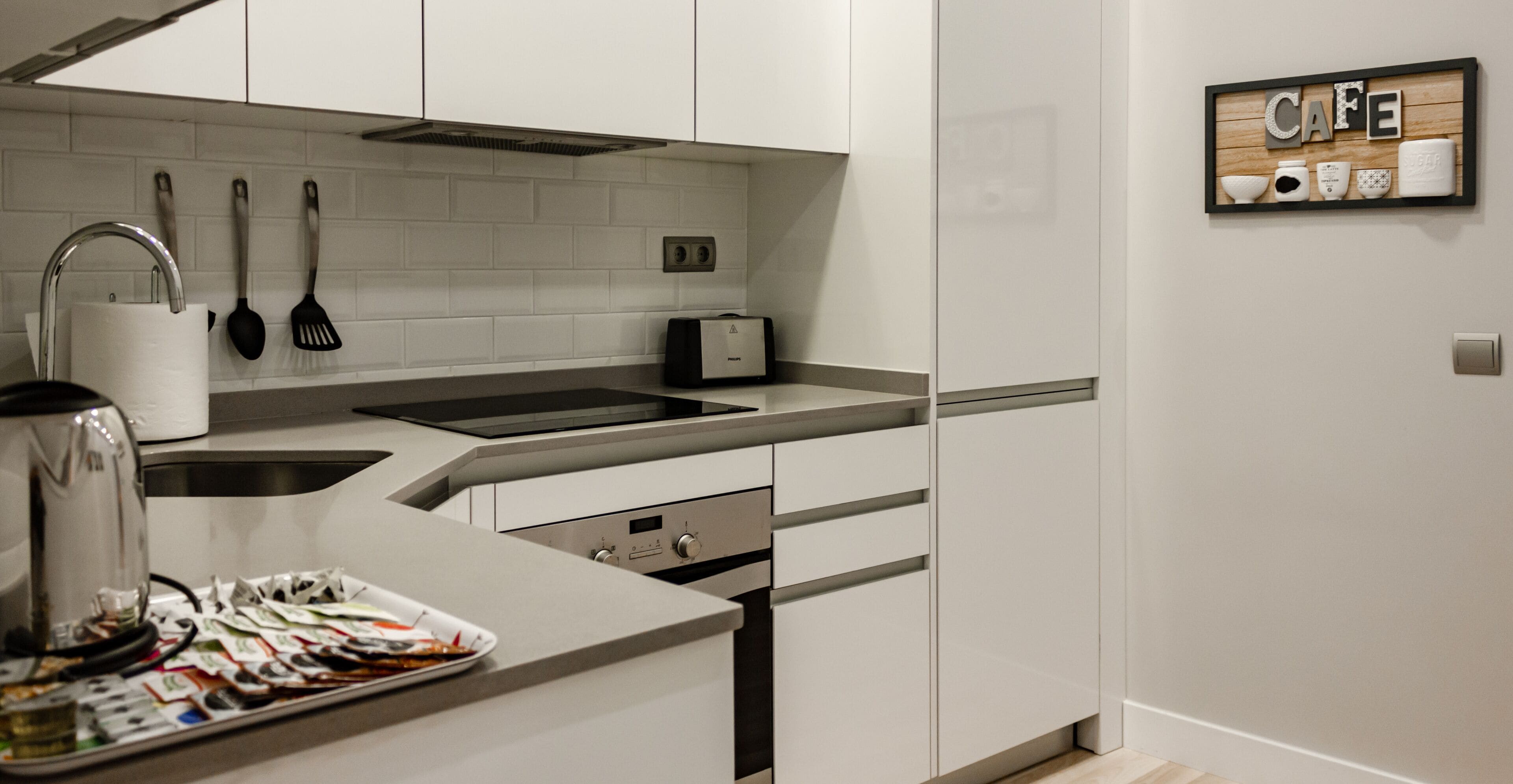 Una cocina moderna con armarios blancos, un lavamanos de acero inoxidable, una cafetera y un tostador.