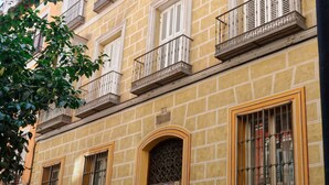 Un edificio de varios pisos con fachada amarilla, ventanas grandes con contraventanas y una entrada central con una puerta decorativa.