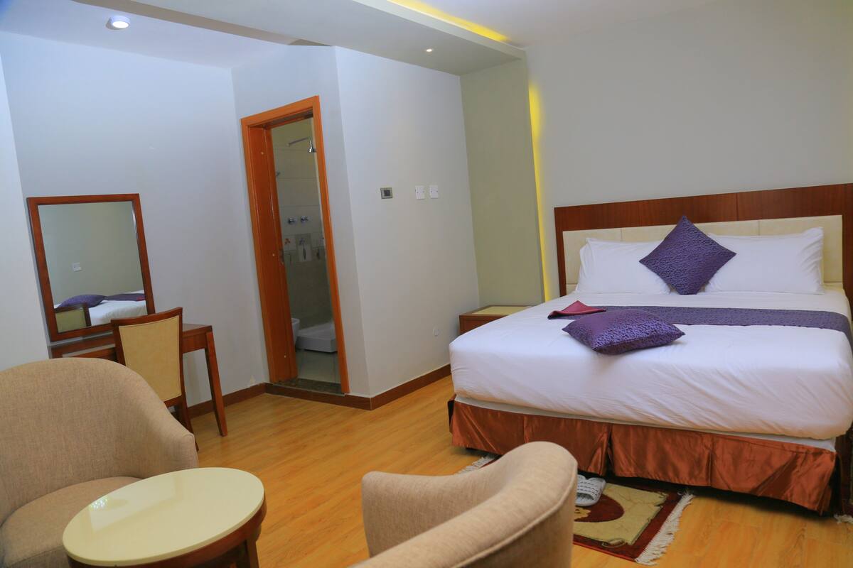 A hotel room with a bed, a chair, a small table, and a mirror.