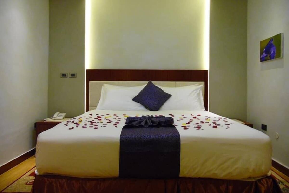 A hotel room with a large bed, a bedside telephone, and a painting on the wall.