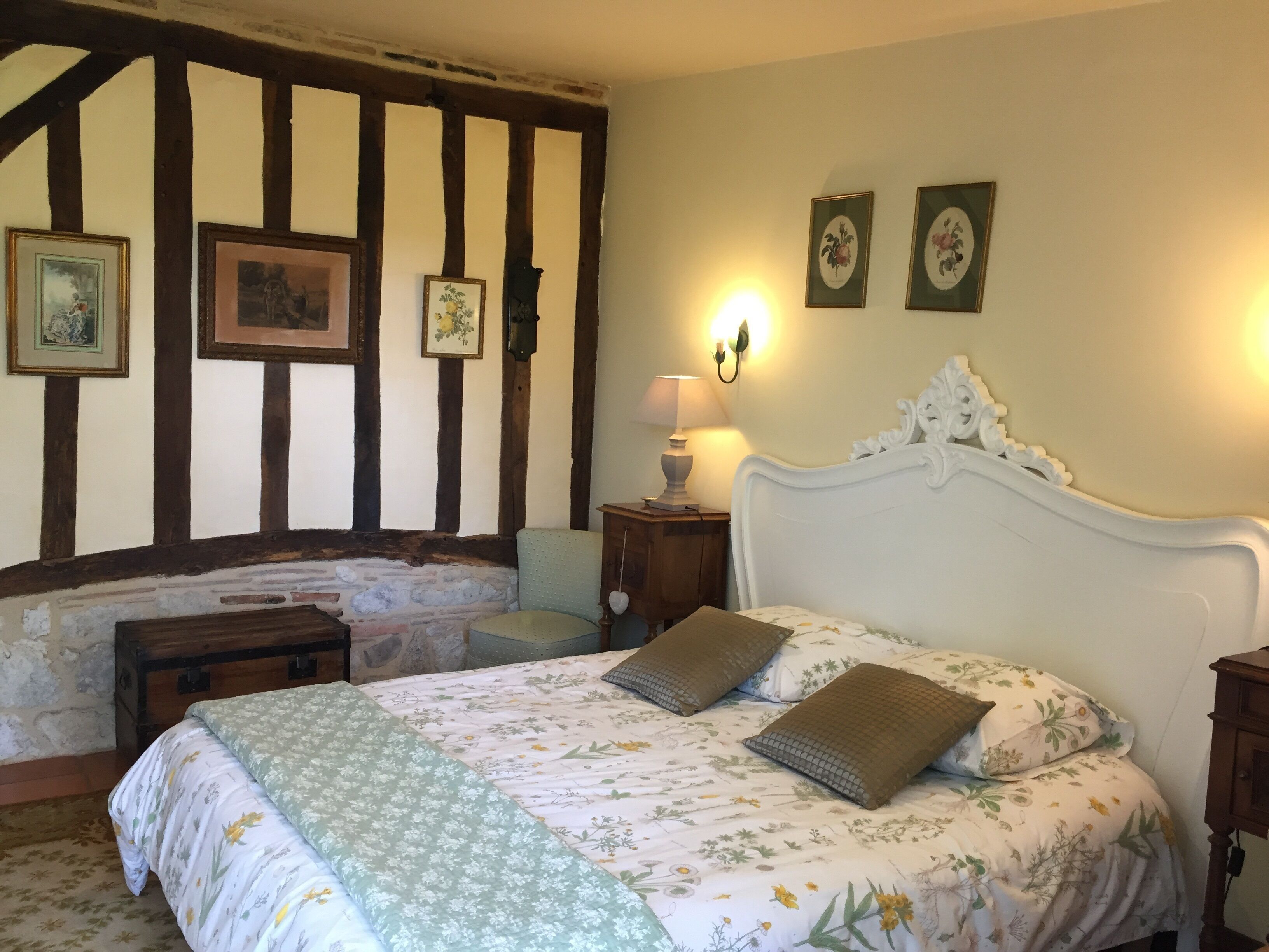 A bedroom with a large bed, a nightstand, a lamp, and a wooden bench.