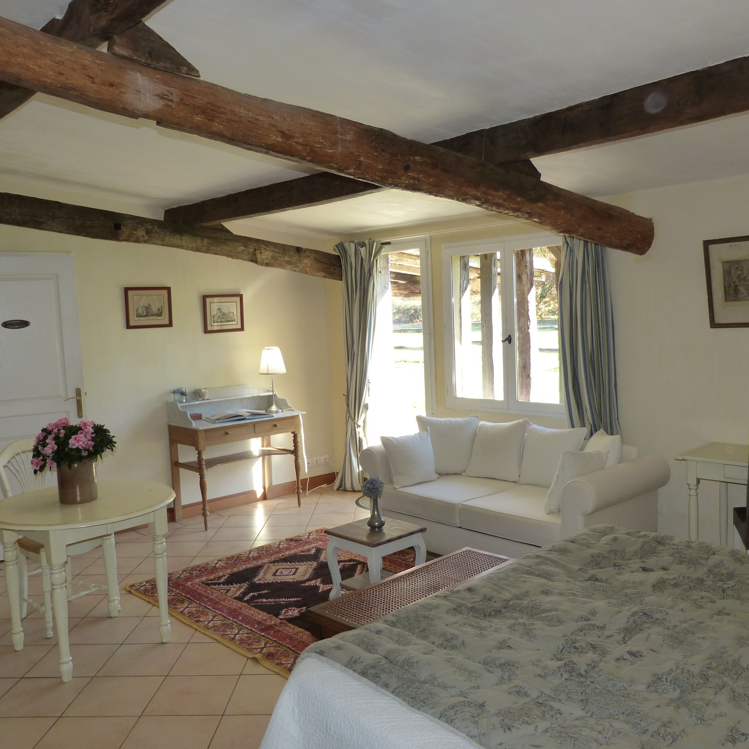 A cozy room with a bed, a white sofa, a desk with a lamp, and a dining table with a chair.