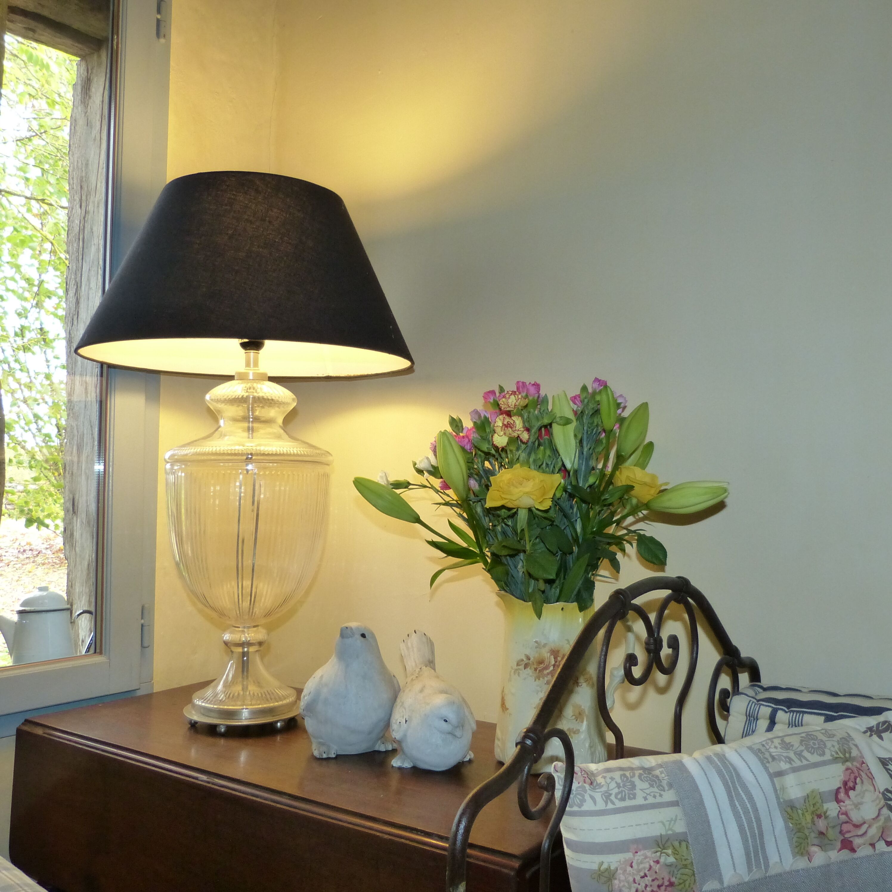 A bedside table with a lamp, a vase with flowers, and two bird figurines.