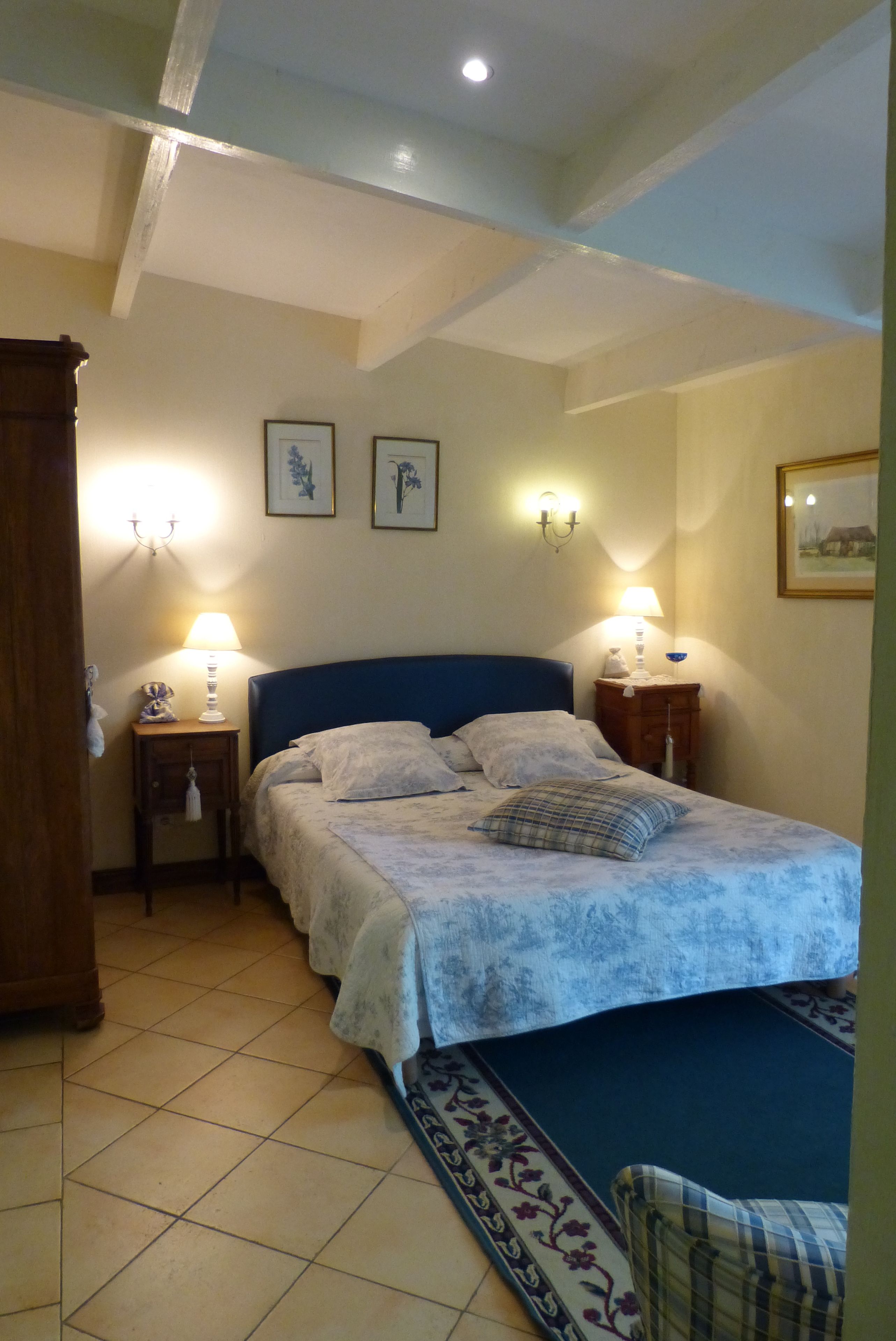 A bedroom with a bed, two bedside tables, a nightstand, a wooden wardrobe, and a framed picture on the wall.