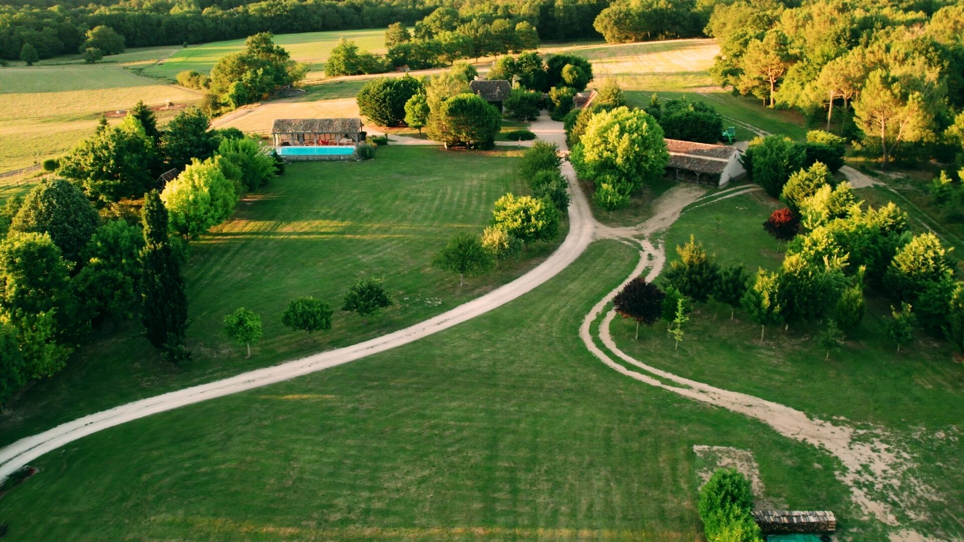 Vista aérea de una propiedad rural con un camino sinuoso, una piscina y varios edificios rodeados de exuberante vegetación.