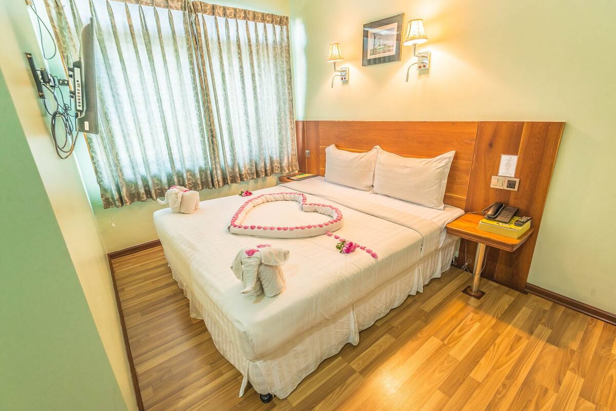 A neatly made bed with a heart-shaped decoration, a bedside telephone, and a nightstand with a lamp.