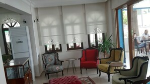 A spacious living room with a red ottoman, patterned rug, and various chairs. - Sevo Hotel (Ayvalik)