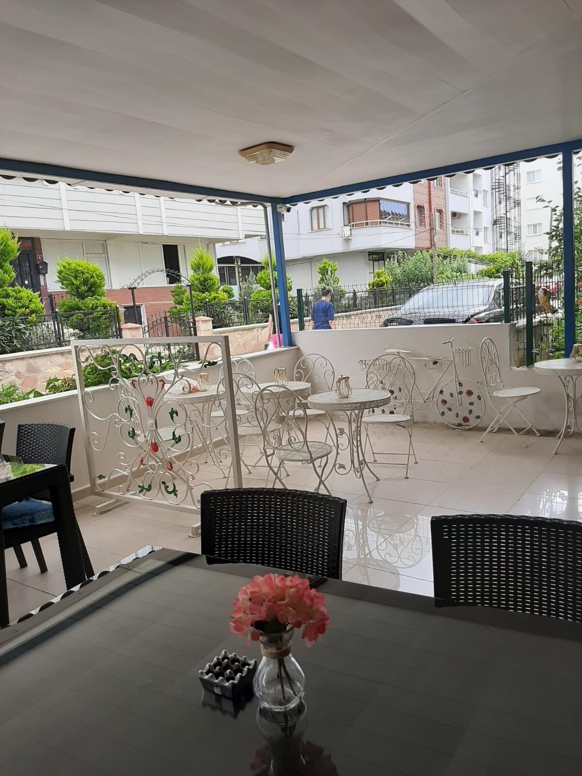 An outdoor seating area with tables and chairs, a decorative fence, and a view of the surrounding buildings.